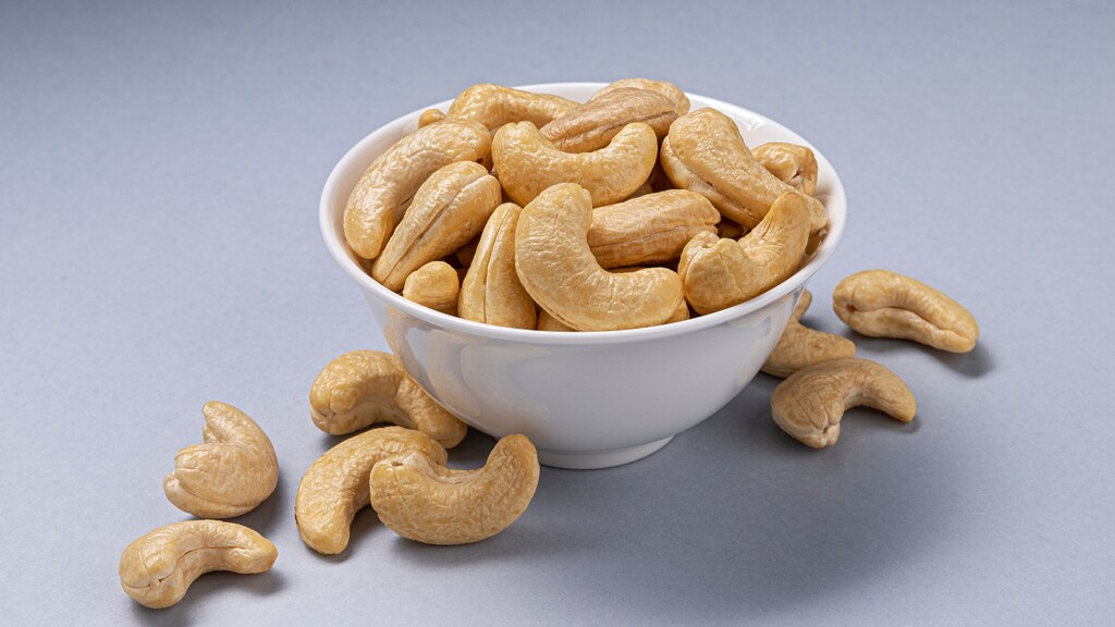 Bowl of cashews with a few cashews scattered on a gray surface.