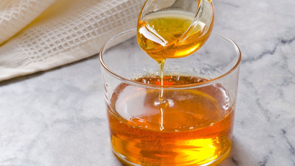 Golden Agave Nectar being poured from a glass pitcher into a small glass bowl on a marble countertop.