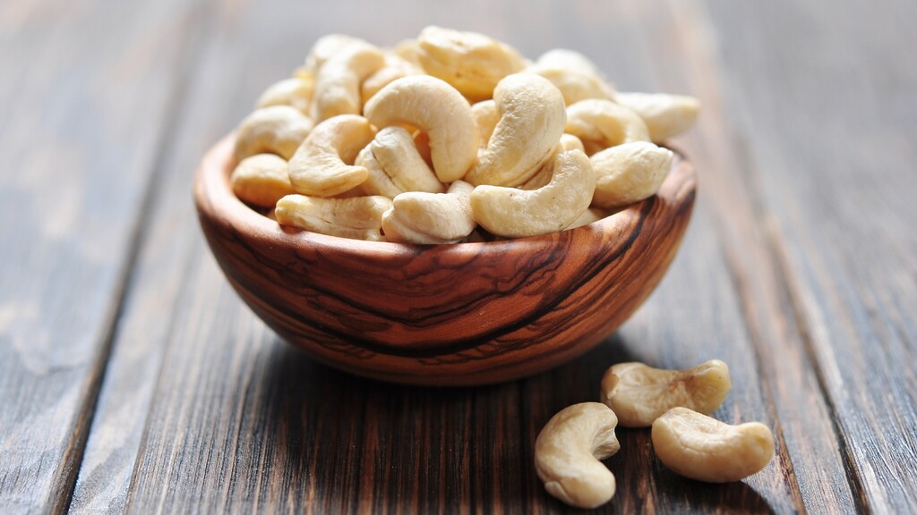 Raw cashews in a wooden bowl on a rustic wooden table.