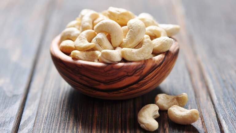 Raw cashews in a wooden bowl on a rustic wooden table.
