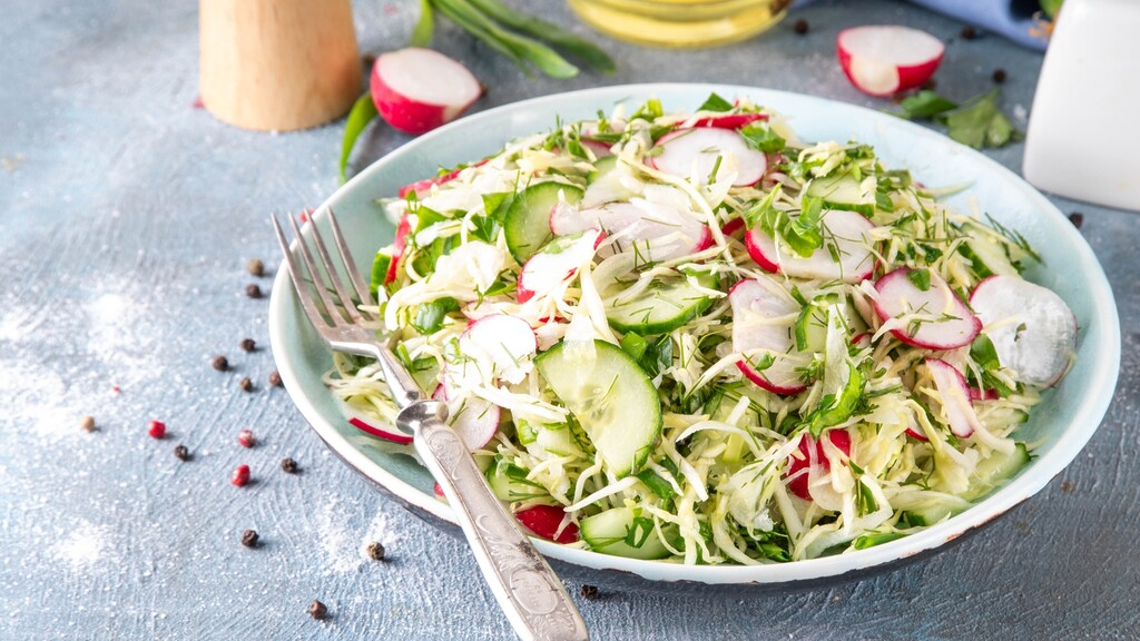 Shredded cabbage, cucumber, radish, and herb salad served on a pale blue plate with a fork.