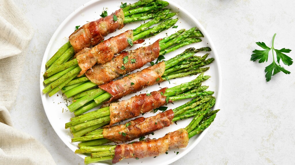 Bacon-wrapped asparagus spears served on a white plate with parsley garnish.
