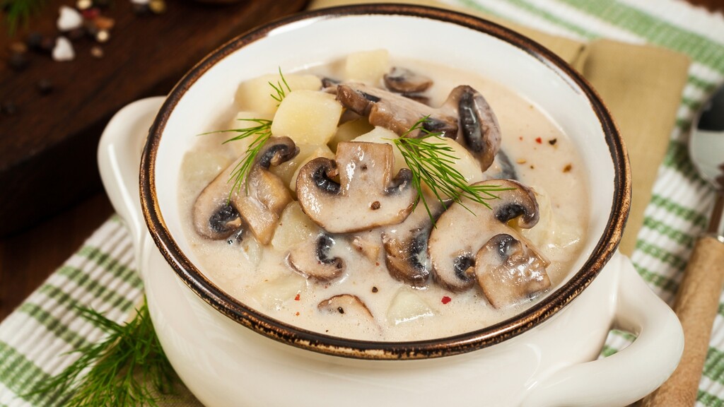 Creamy mushroom and potato soup garnished with fresh dill in a handled bowl.