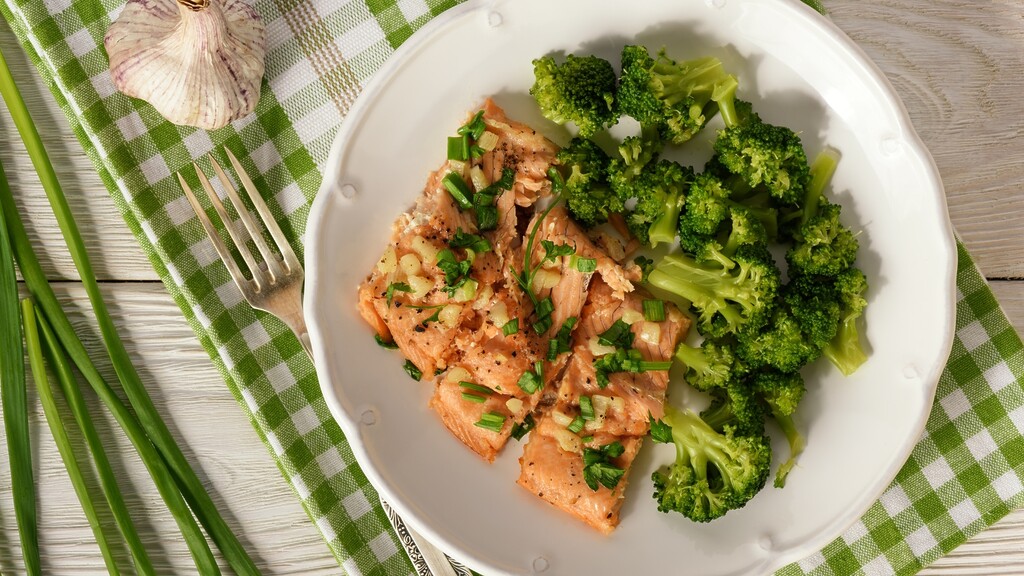 Plate of cooked salmon with broccoli on a white table.