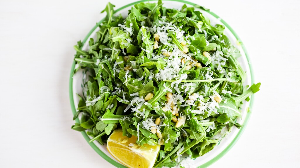 Arugula salad topped with grated cheese and pine nuts, served with a lemon wedge.