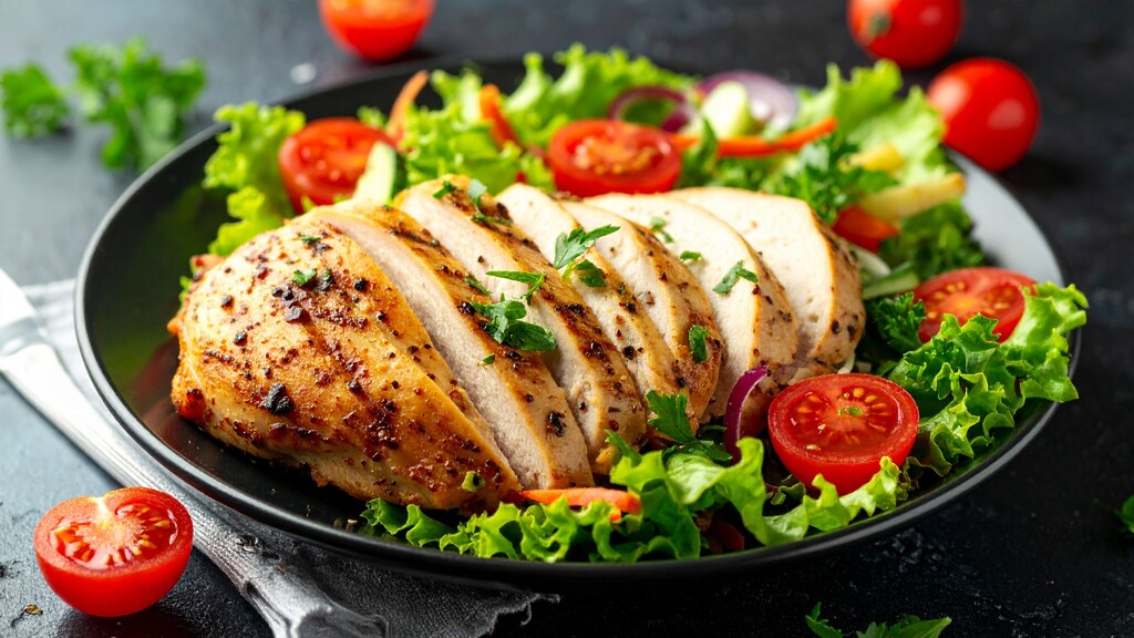 Grilled chicken breast served over a fresh salad with lettuce, tomatoes, herbs, and sliced vegetables.