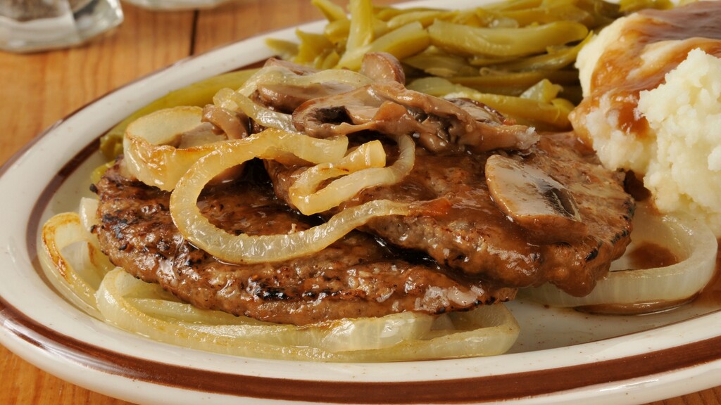 Grilled steak with onion rings, mushrooms, gravy, mashed potatoes, and green beans on a plate.