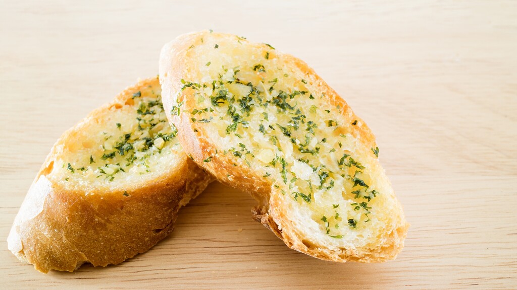 Two slices of garlic bread topped with herbs on a light wooden surface.