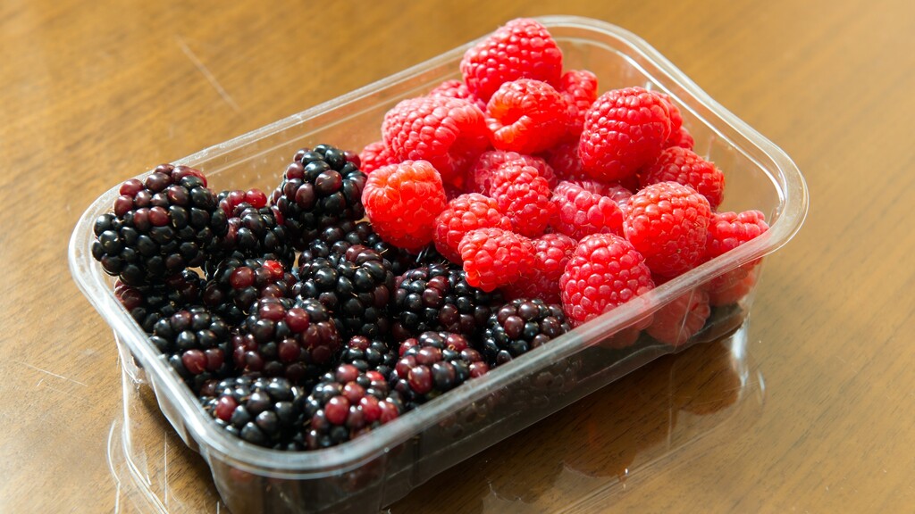 Mixed berries: Plastic container filled with blackberries and raspberries on a wooden table.