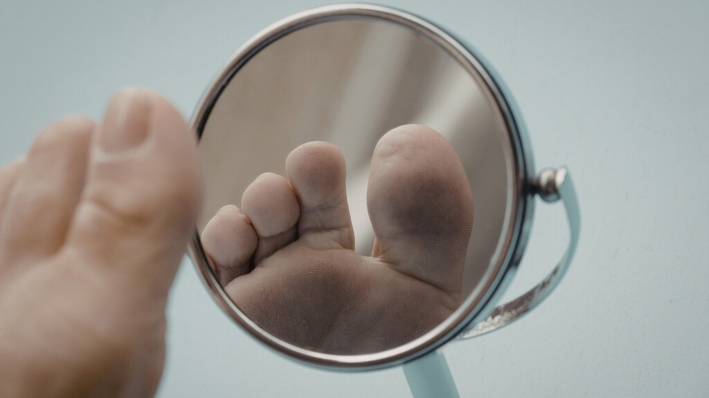 Close-up of a foot reflected in a round mirror, highlighting the sole and toes.