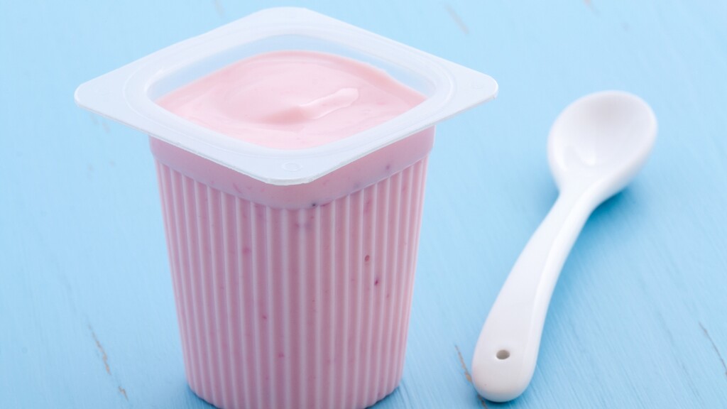 Pink yogurt cup with a white spoon on a blue surface.