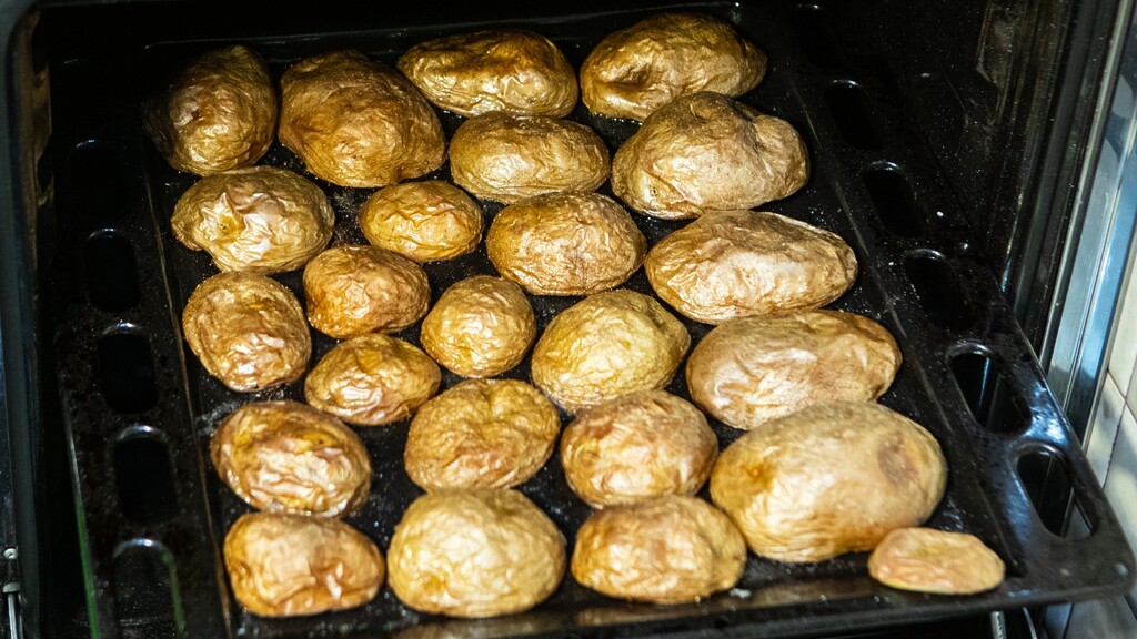 Roasted potatoes: Tray of golden roasted potatoes inside an oven.