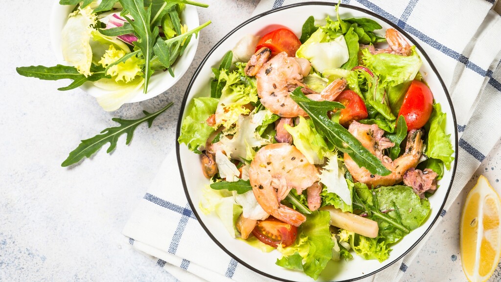 Shrimp salad with leafy greens, cherry tomatoes, and lemon wedges on a table setting.