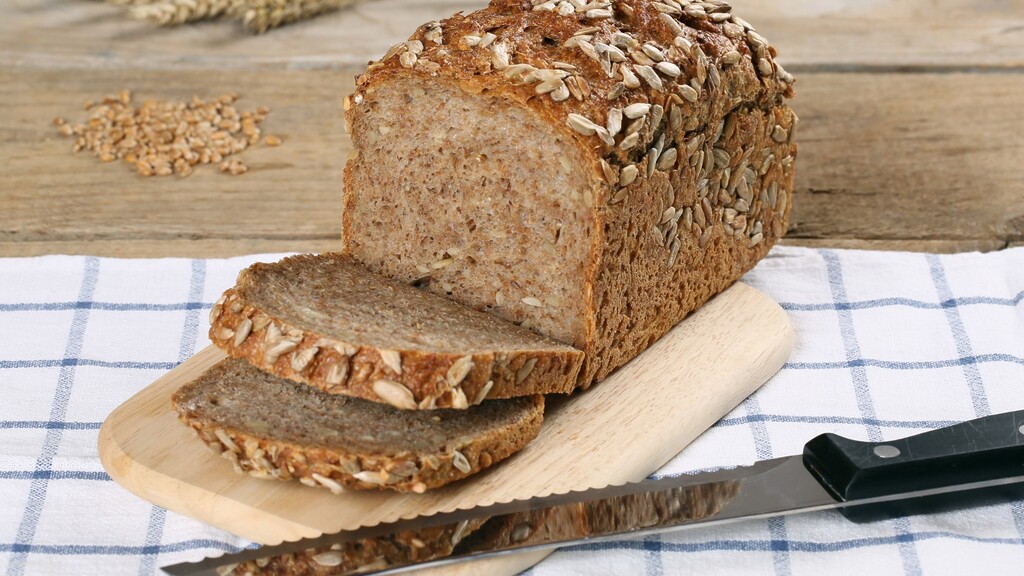 Seeded bread: Sliced loaf of seeded bread on a cutting board with a bread knife beside it.