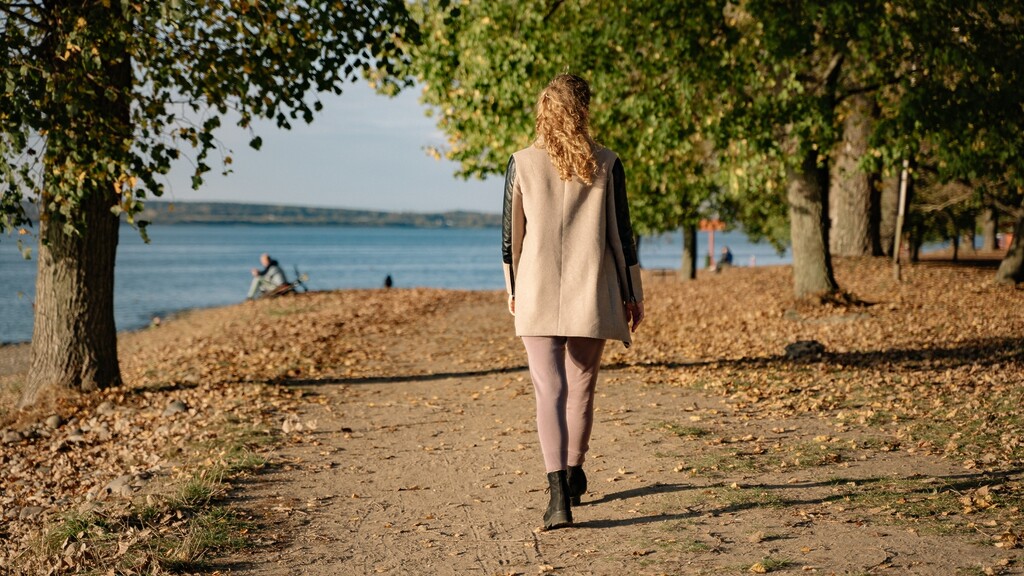Woman taking a low-stress walk on a tree-lined path by the water.