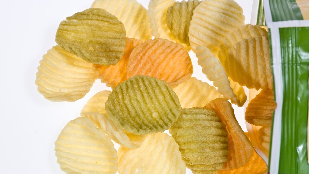 Ridged vegetable chips spilling near a green snack bag on a white background.