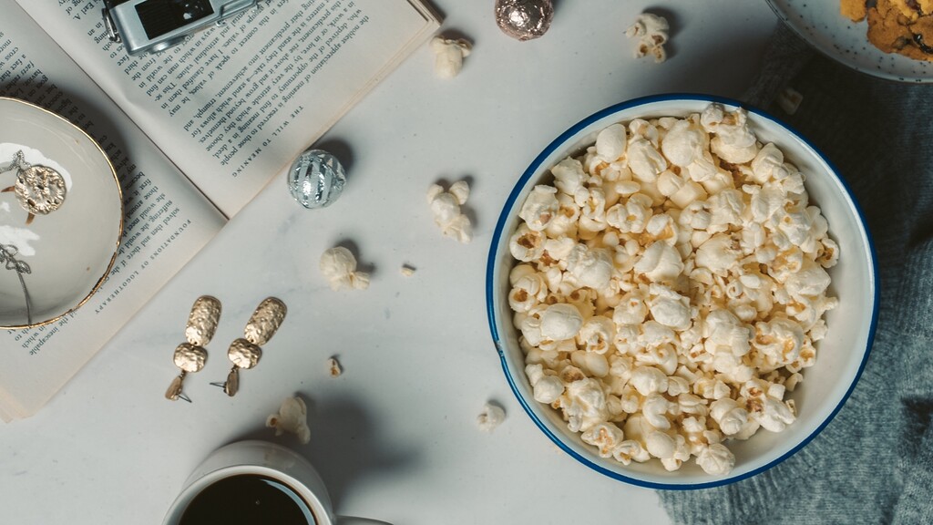 Bowl of popcorn beside books and tea.