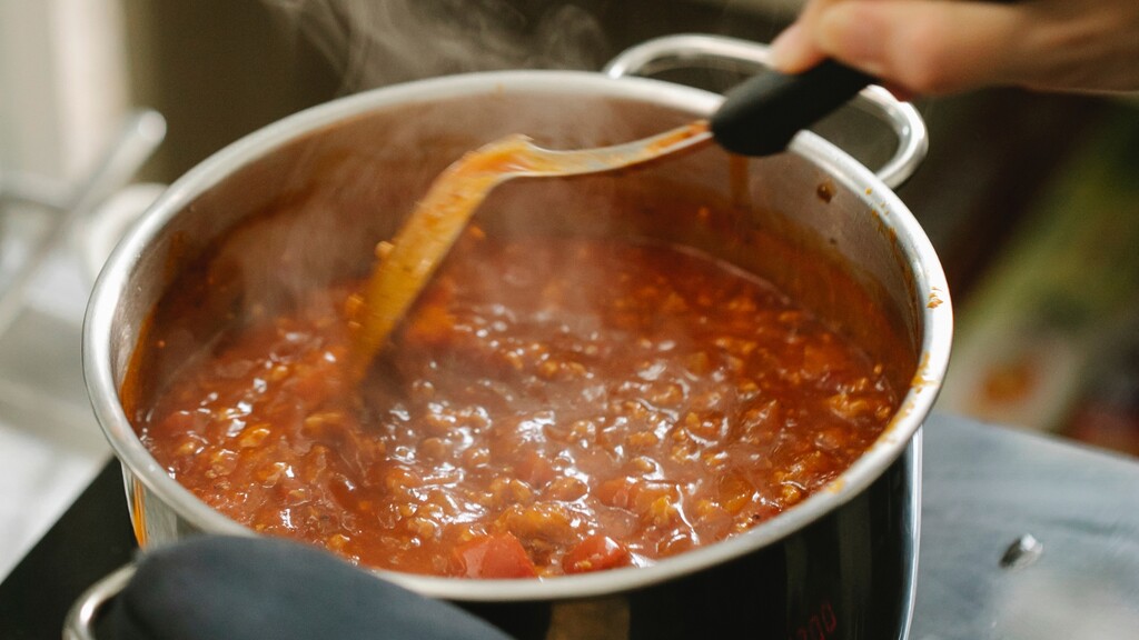 Tomato sauce: Pot of simmering tomato sauce being stirred with a spoon.