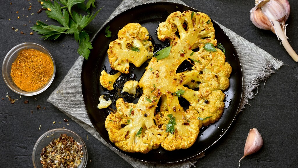 Roasted cauliflower steaks seasoned with spices, garnished with parsley and garlic.