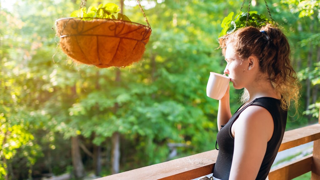 Woman drinking tea on a porch surrounded by greenery.