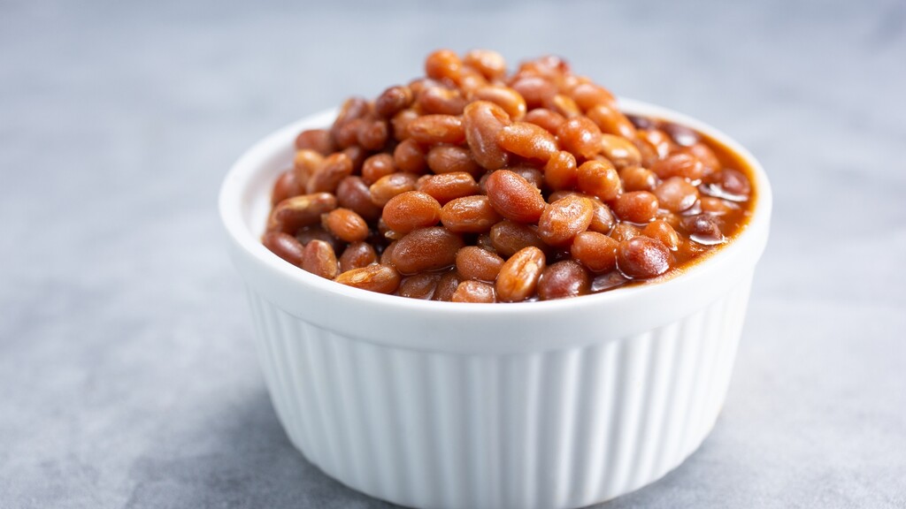 Bowl of baked beans in tomato sauce on a light gray background.