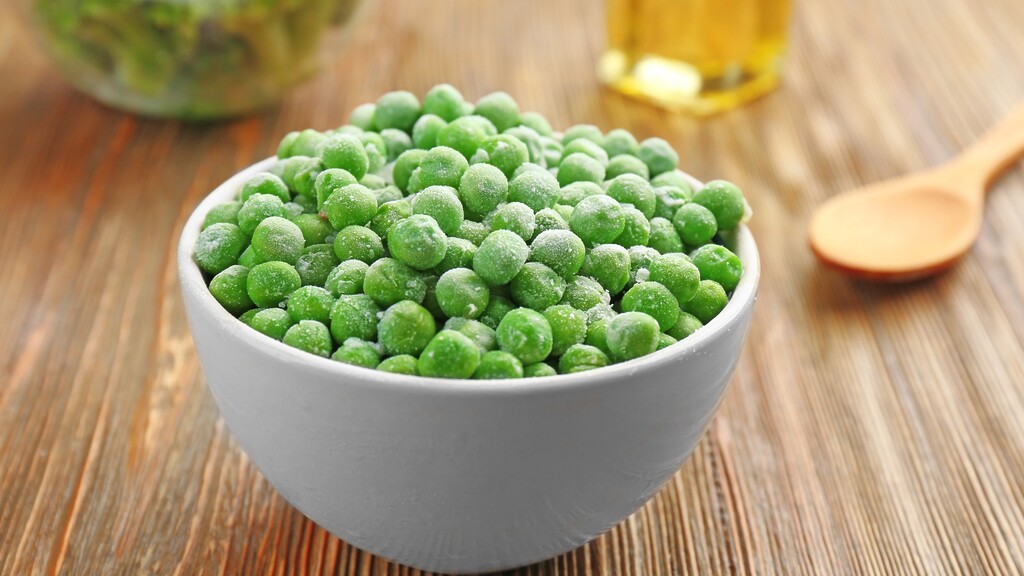 Frozen peas: White bowl filled with frozen green peas on a wooden surface.