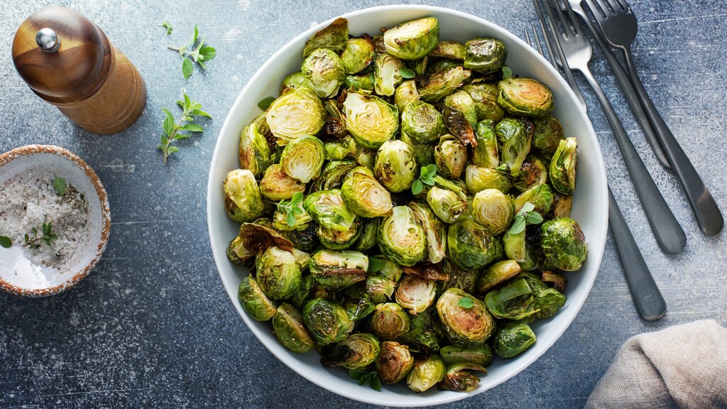Roasted Brussels sprouts served in a white oval dish with herbs and seasoning.