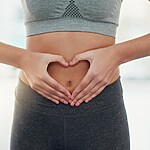 Person forming a heart shape with their hands over their stomach, symbolizing gut health and digestive care.