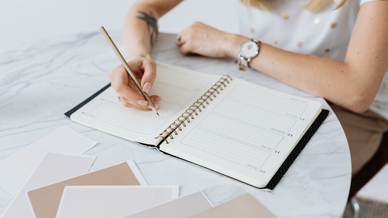 Person writing in a planner on a marble table.
