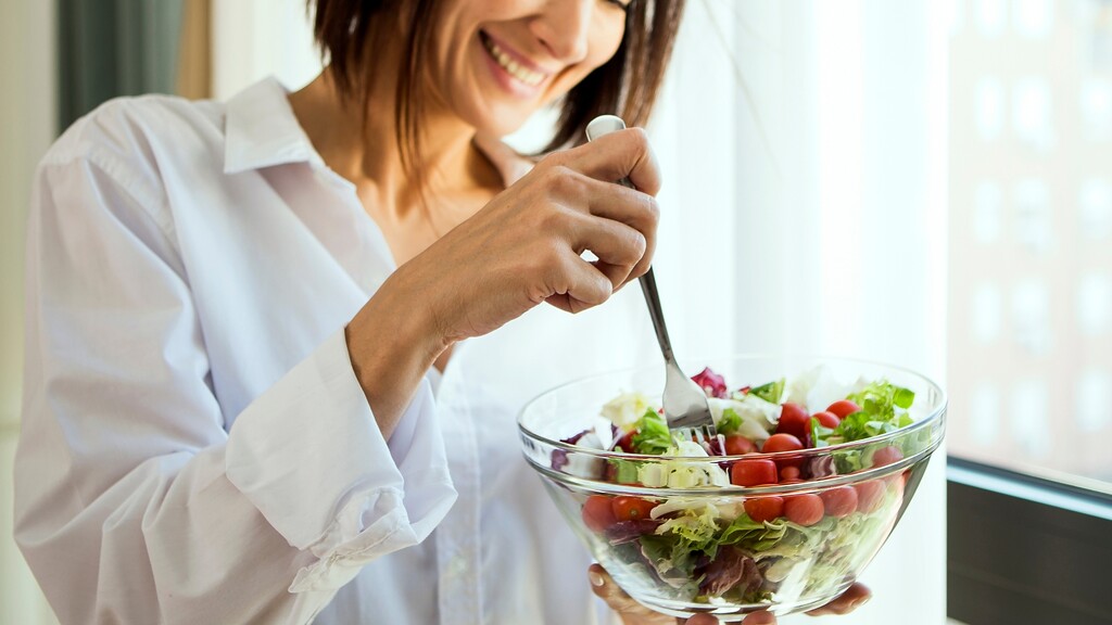 Woman eating a fresh salad by a window.