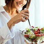 8 Simple Ways to Transition to a Gut-Friendly Lifestyle Woman eating a fresh salad by a window.