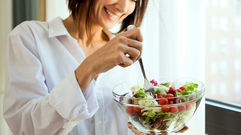 Woman eating a fresh salad by a window.