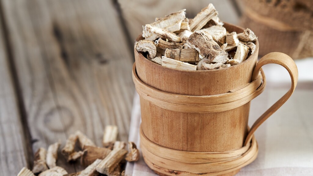 Dried marshmallow root pieces in a small wooden bucket on a rustic wooden surface.