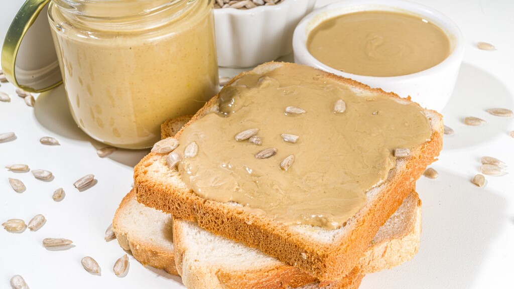 Toast spread with sunflower seed butter beside a jar and scattered seeds.