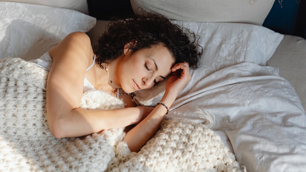 Woman sleeping peacefully under a cozy blanket to support overnight skin repair and restful recovery.