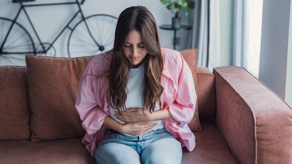 Woman sitting on a couch and holding her stomach.