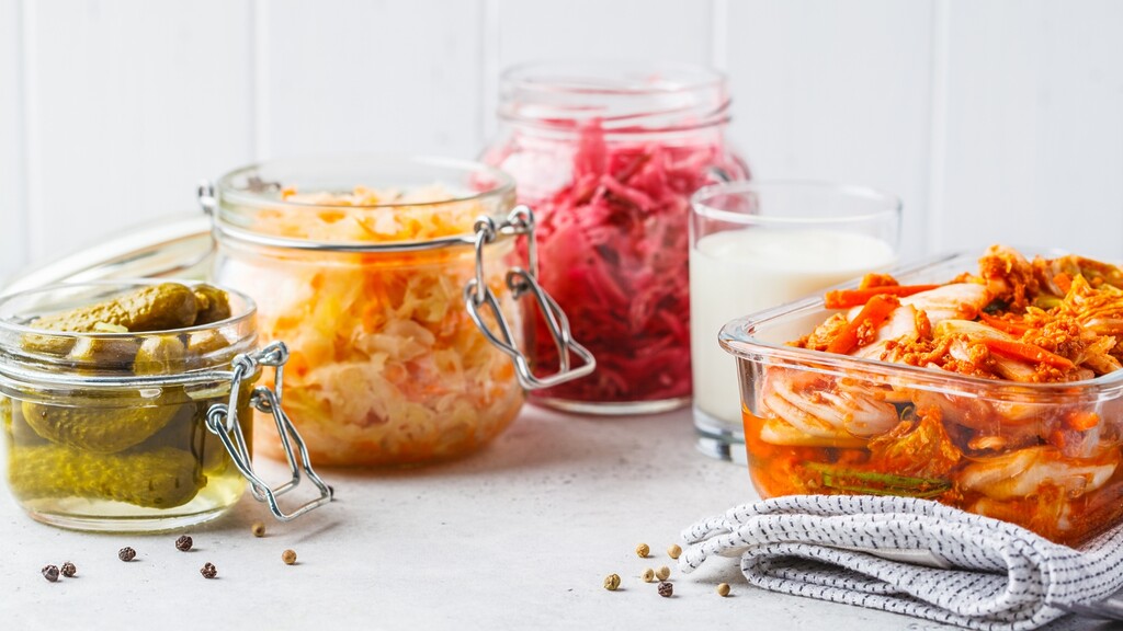 Assorted fermented foods on a kitchen counter, including sauerkraut, kimchi, pickles, and kefir.