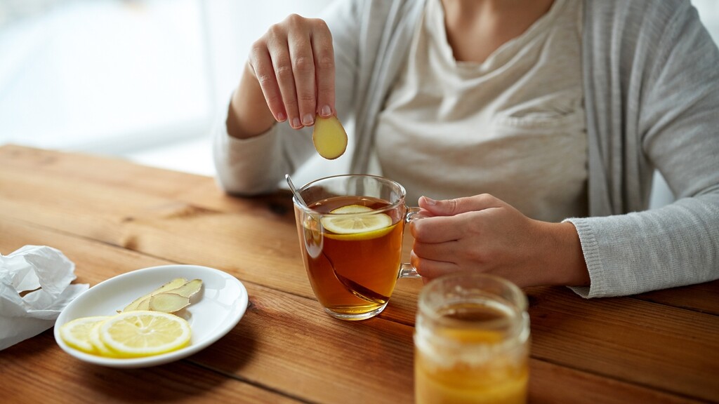 Person adding lemon to a cup of tea on a wooden table.