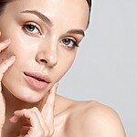 5 Unexpected Perks of Prebiotics (And Why My Skin Finally Cleared Up) Woman with clear skin gently touching her face against a plain light background.