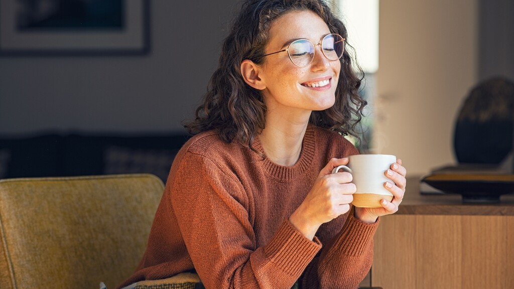 A woman holds a mug while sitting indoors in warm natural light.