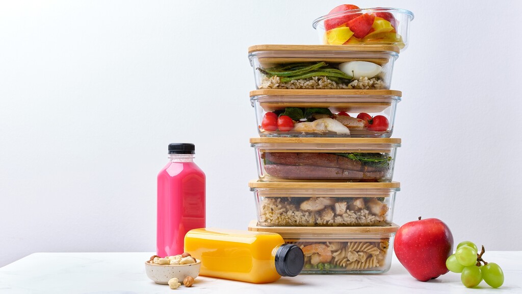 Stacked glass meal prep containers filled with balanced meals, fruit, and snacks.