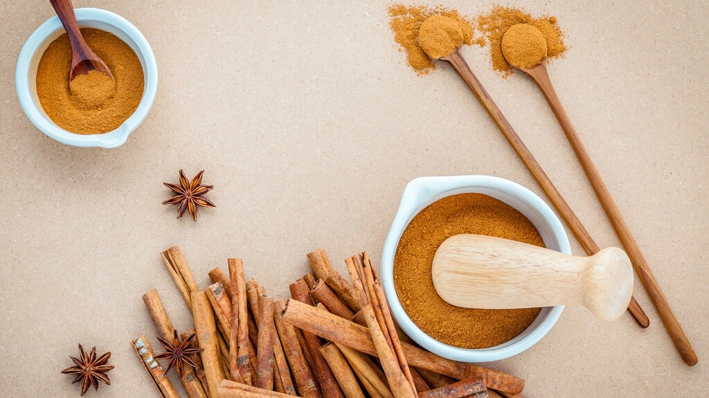 Cinnamon sticks, ground cinnamon, and wooden spoons arranged on a neutral surface.