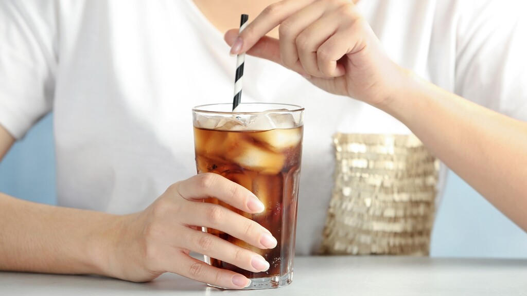 A person stirring a glass of iced soda or sweetened tea with a straw.