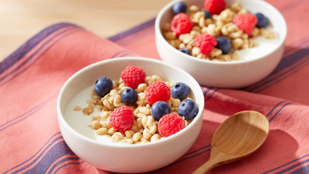 Two bowls of yogurt topped with raspberries, blueberries, and granola.