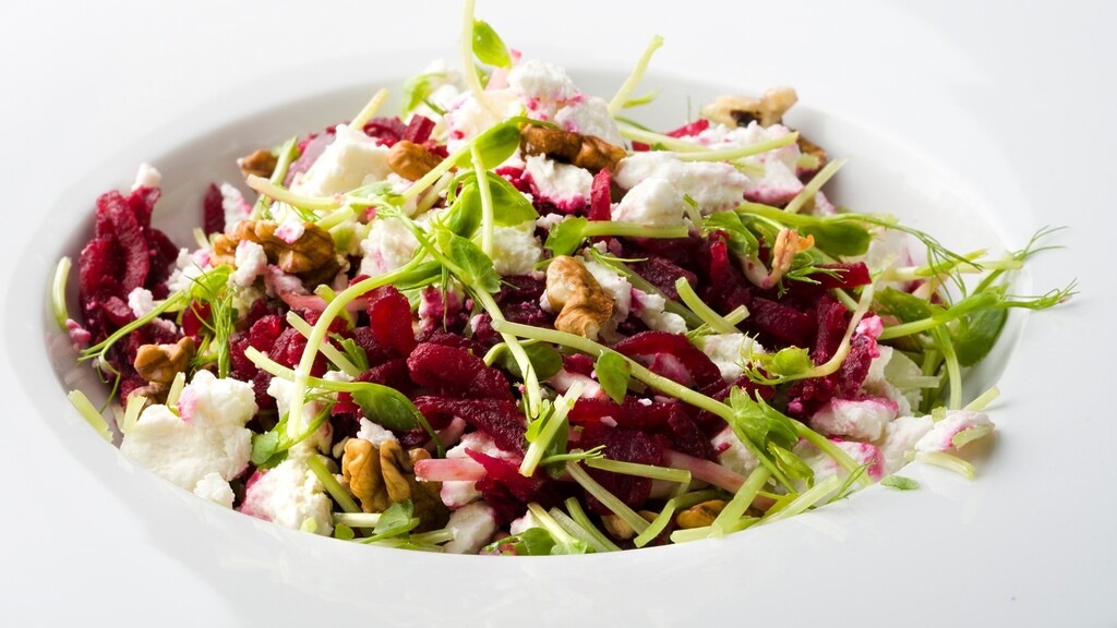 A beet, walnut, greens, and cheese salad served in a white bowl.
