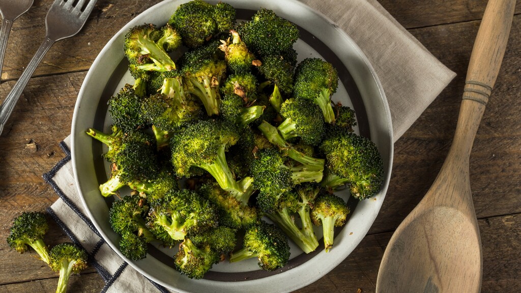 Roasted broccoli florets served in a bowl beside a wooden spoon.