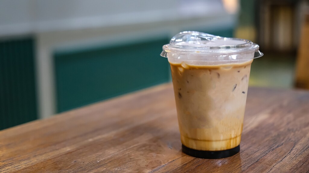 An iced coffee drink in a clear plastic cup on a wooden table.