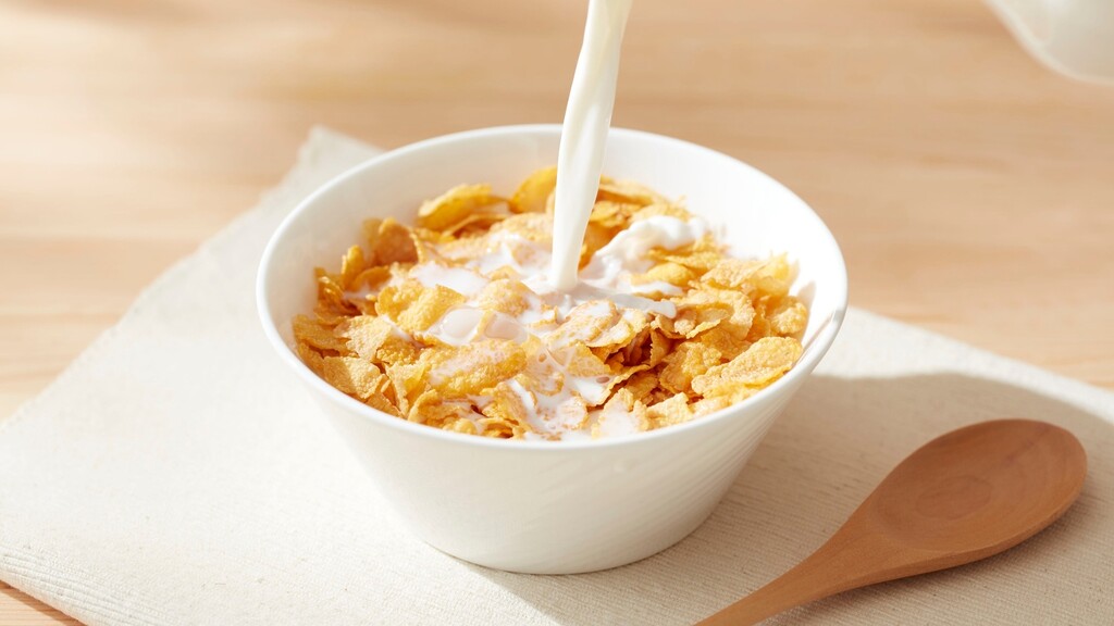 Milk being poured into a bowl of breakfast cereal beside a wooden spoon.