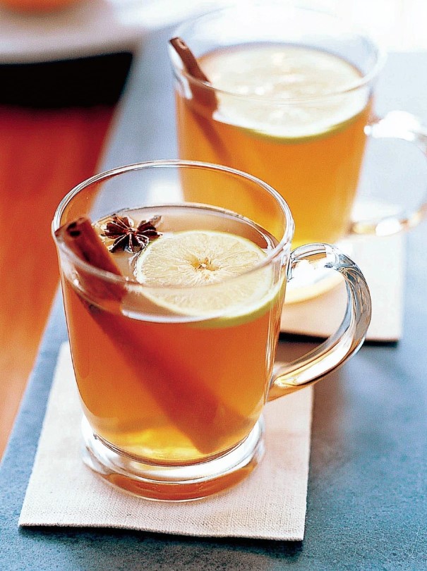 Sugar-free cinnamon tea - Two clear mugs of amber spiced tea garnished with fresh lemon slices, cinnamon sticks, and star anise on a cozy wooden table.