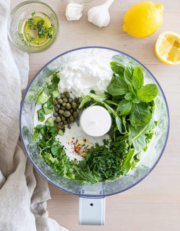 The preparation stage showing all ingredients—avocado, herbs, yogurt—placed inside the food processor before blending.